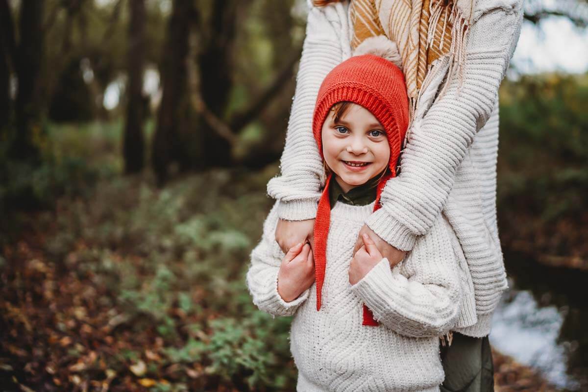 A little girl smiling at the camera and wearing a hat bobble hat for a oxford family photographer