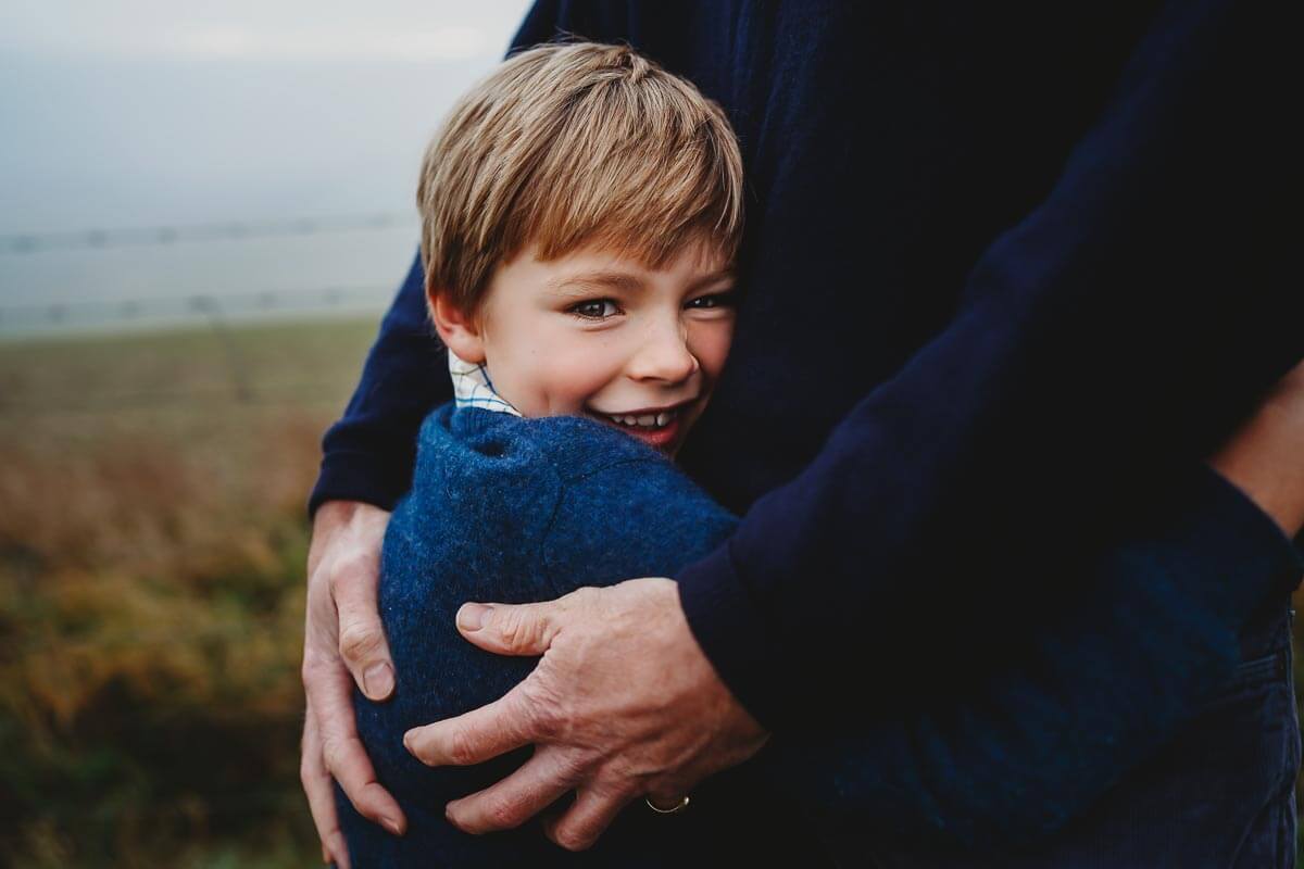 a boy cuddling his dads side and smiling for a marlborough photo shoot