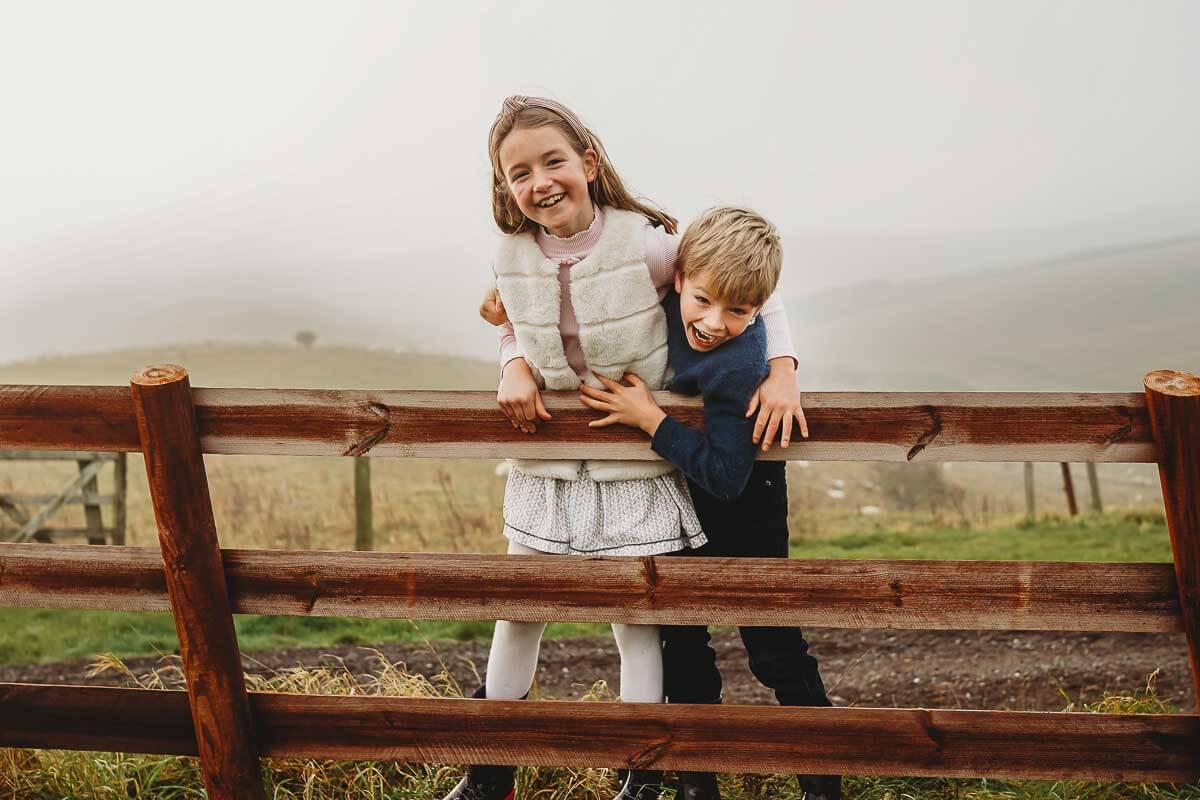 brother and sister playing around on a gate in Marlborough for a family photographer 