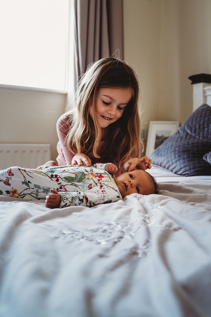 A Newbury lifestyle photoshoot of a sister stroking her newborn sister