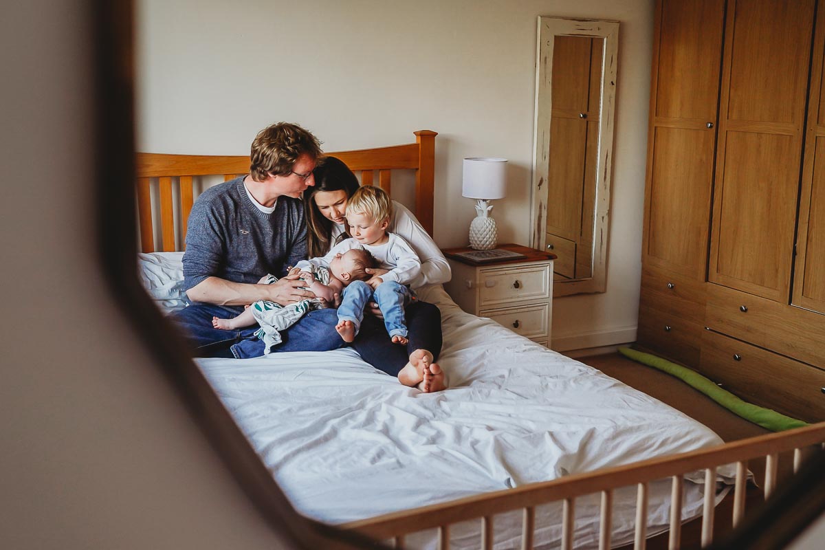 Family cuddling their newborn on their bed during an in home photoshoot