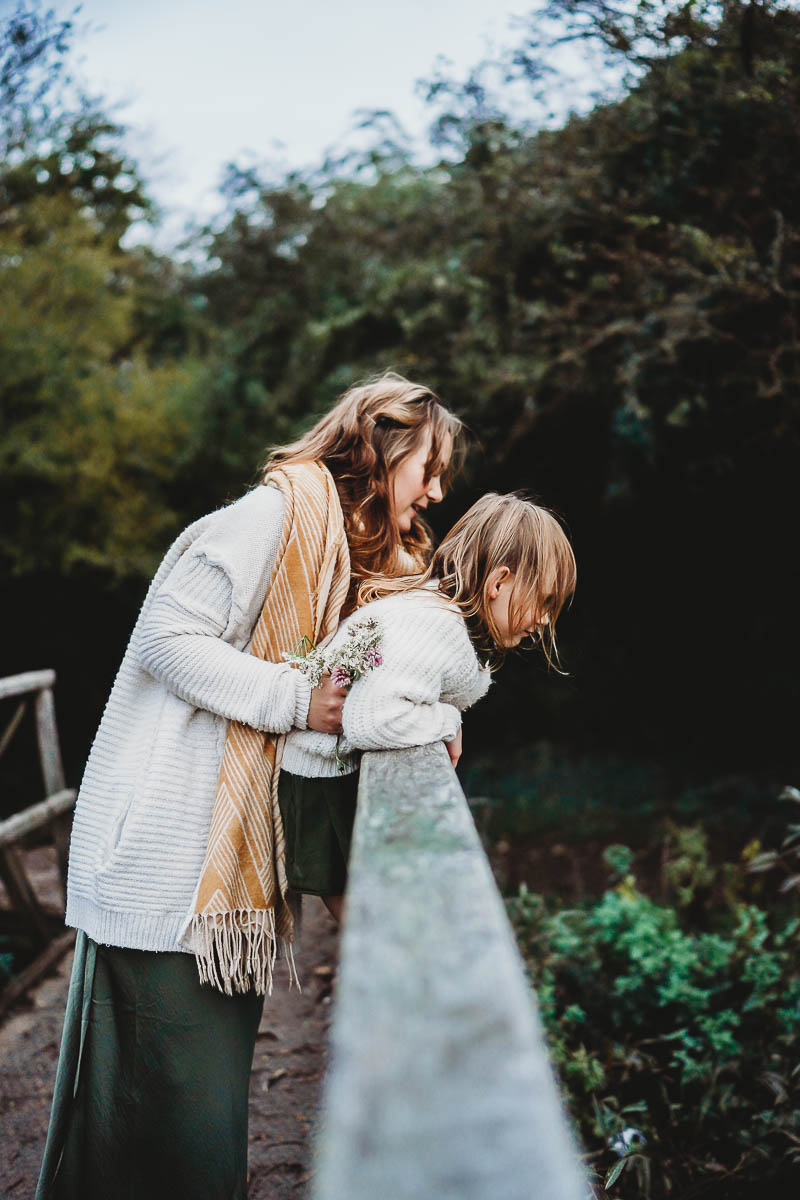 a mother and daughter looking over a bridge of a stream 