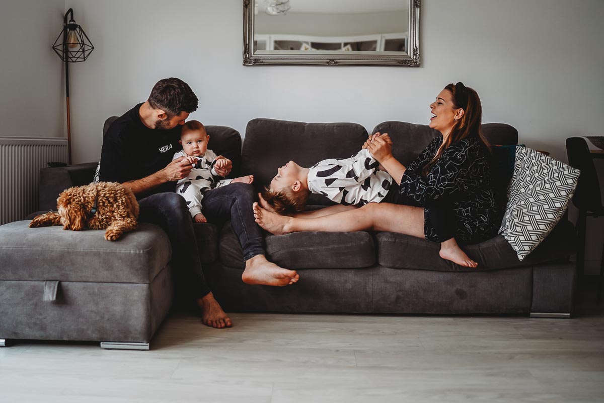 A family playing and cuddling together on a sofa during an in home newborn photoshoot