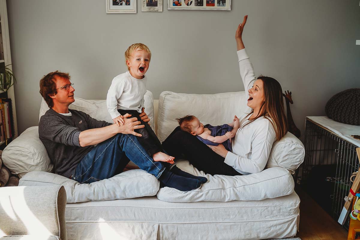 a family playing on the sofa in their Newbury home during as instructed by a newborn photographer