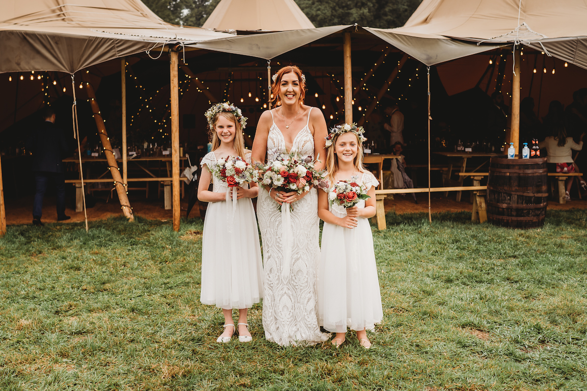 a bride with her 2 flower girls posing in front of her wedding tipis