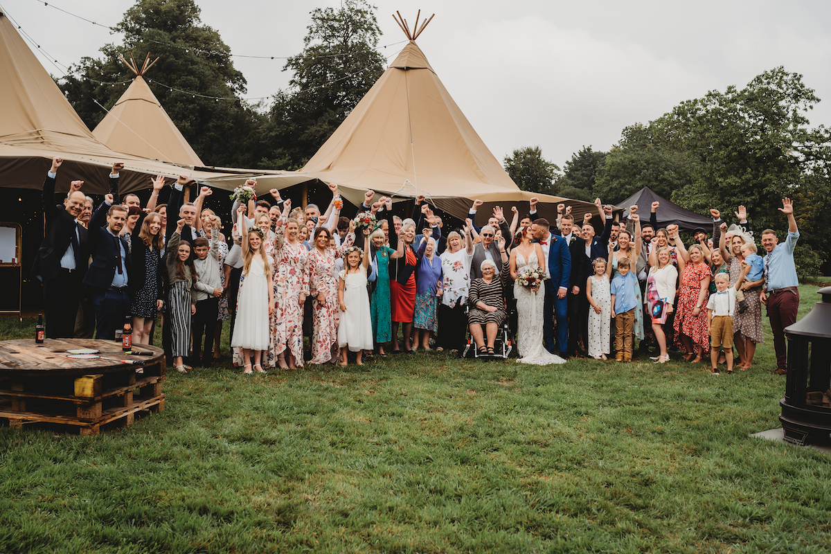 full wedding party cheering as the bride and groom kiss