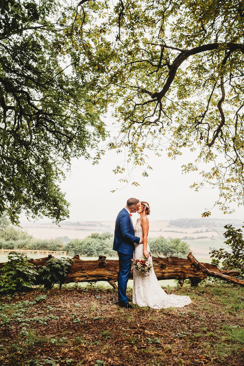 a bride & groom kissing in front of a beautiful backdrop taken by a newbury wedding photographer