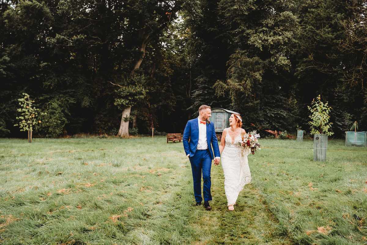 a bride & groom laughing together as they stroll  across a field