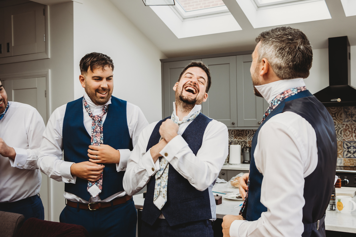 groom laughing as he tries to tie his tie before his wedding in Berkshire