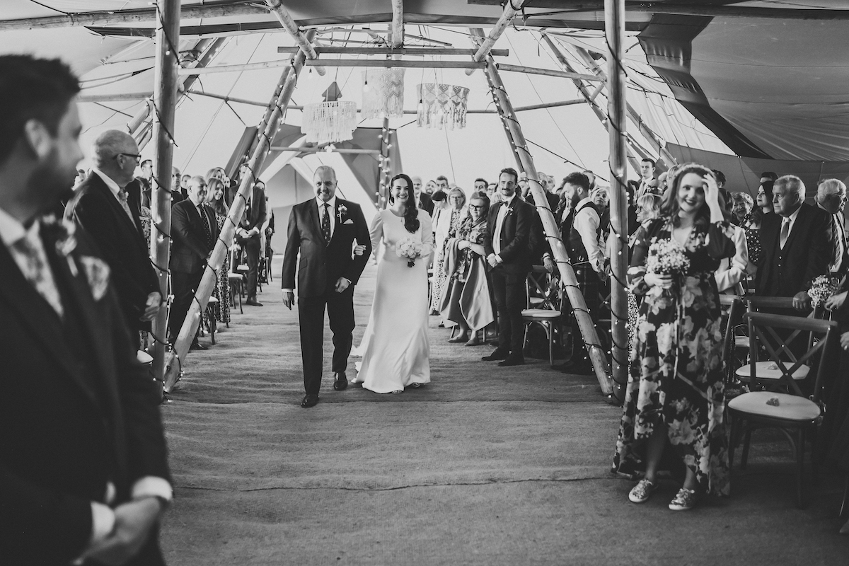 a bride and her father walking down the aisle forest edge tipis