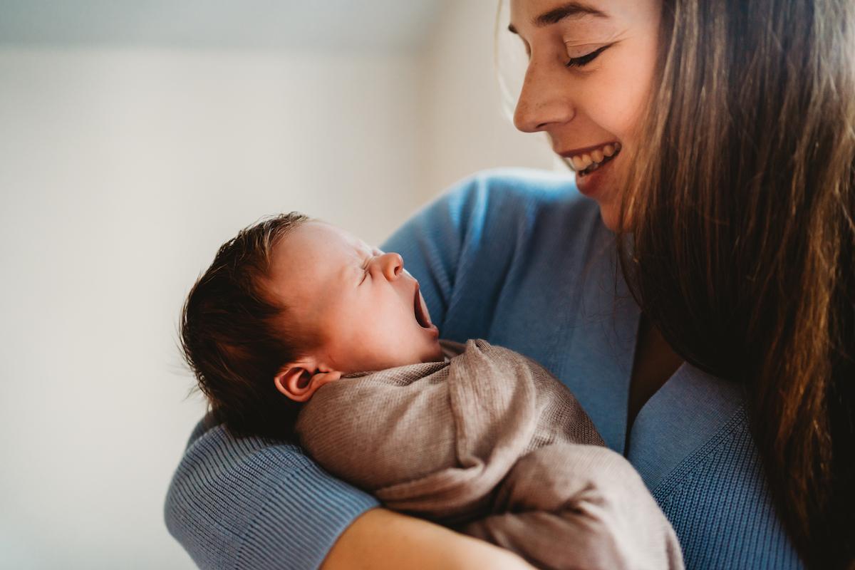 a newborn baby yawning as her mum smiles on during for a baby photographer newbury