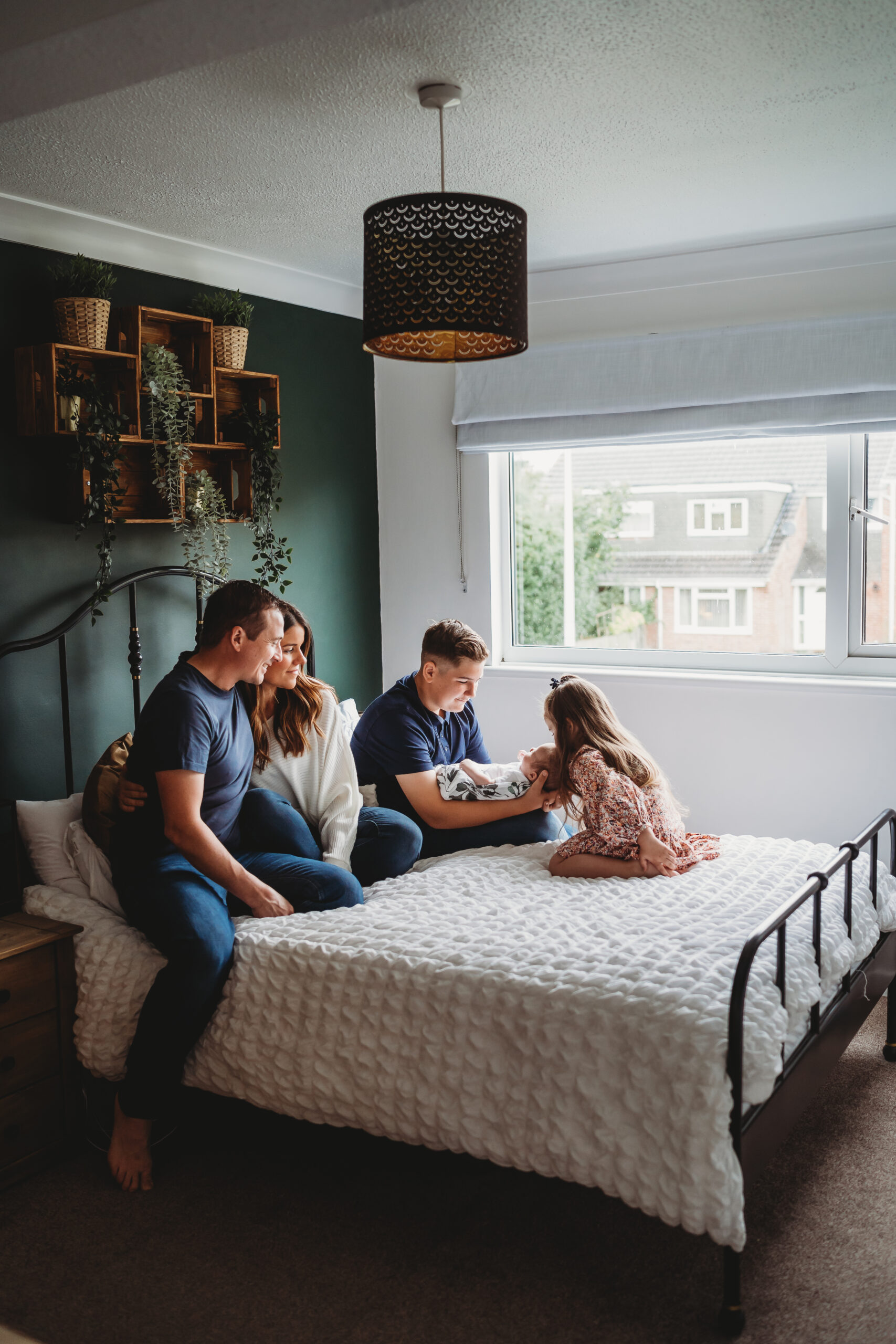 A family cuddled on the bed as their daughter kisses a newborn on her head for a newbury photographer