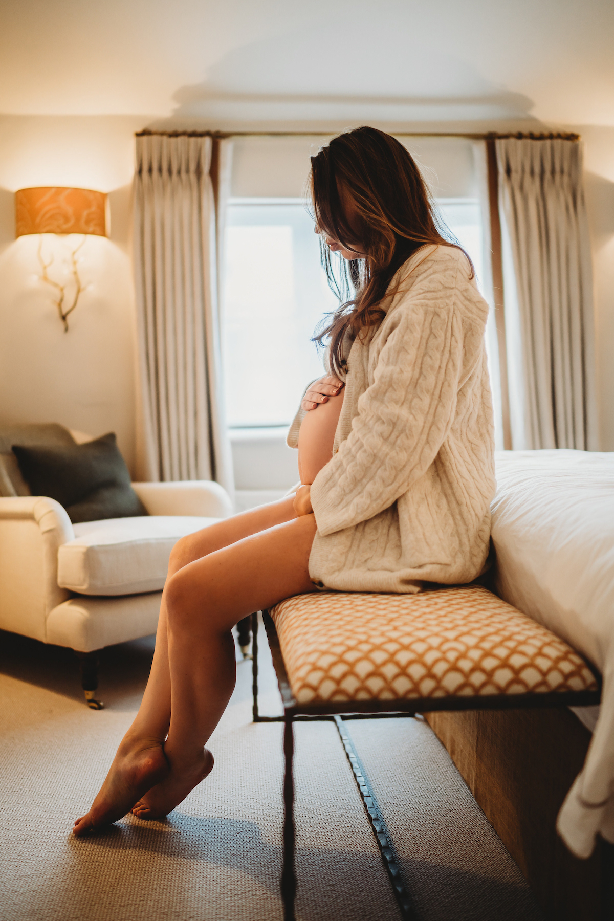 A pregnant lady sat at the end of her bed holding her bump for a Newbury pregnancy photographer