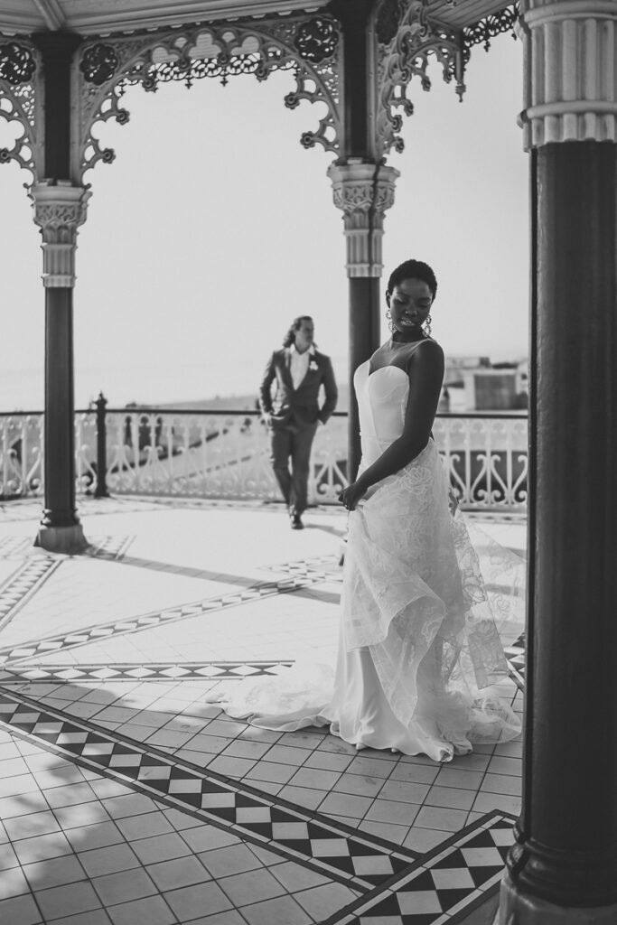 a black and white image of a bride standing on Brighton Pier as her husband looks on