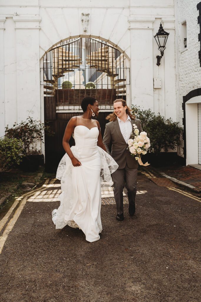 a married couple running through the streets of Brighton after their city elopement. The groom hokding the flowers as they look at each other