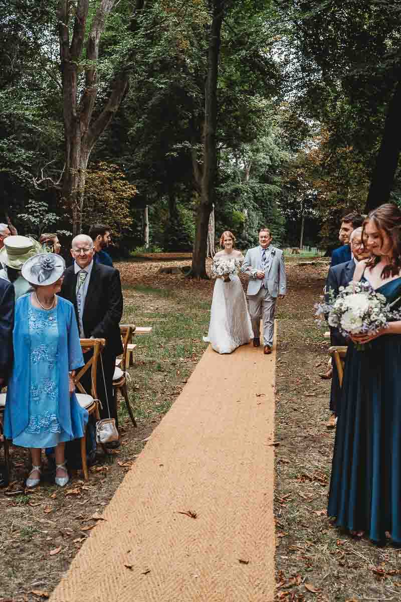 a father of the bride walking his daughter down the aisle of their woodland ceremony taken by a berkshire wedding photographer