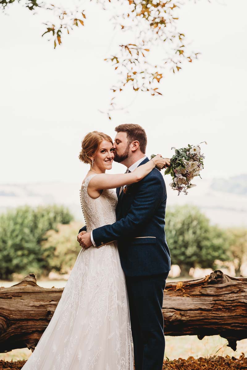 a bride and groom cuddling in front of a stunning back drop for a berkshire wedding photographer 