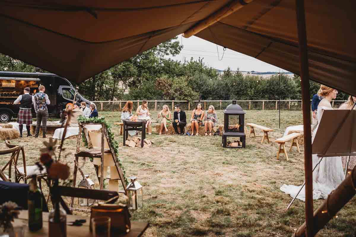 wedding guests lined up and sat on hay bales whilst eating pizza taken by a oxfordshire wedding photographer