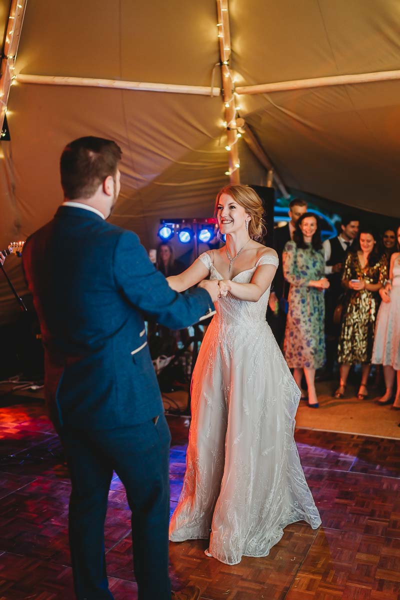 a bride and groom smiling and dancing whilst at a forest edge tipi wedding