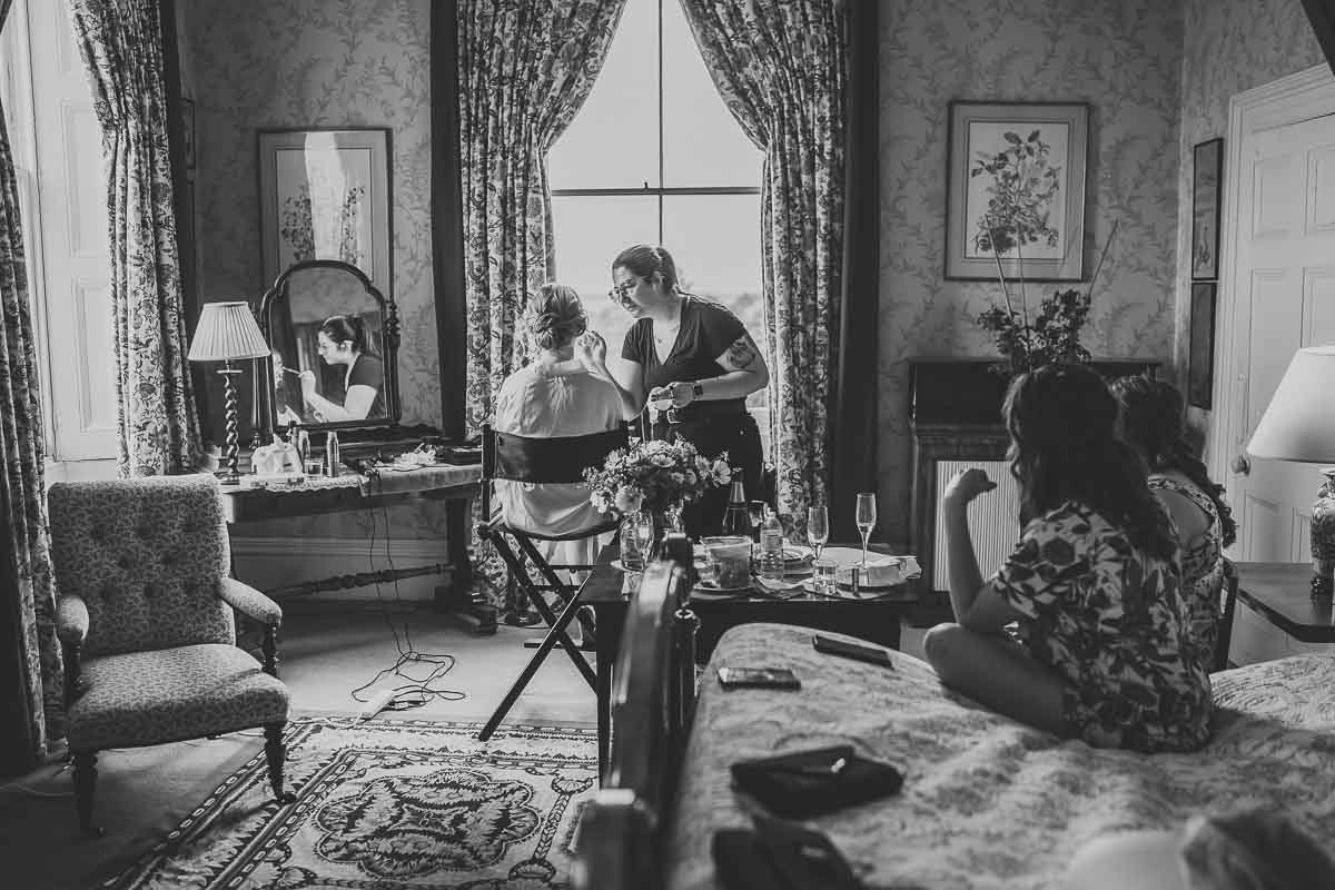 a black and white photo of a bride and her bridesmaids having their make up done ahead of her woolley park estate wedding