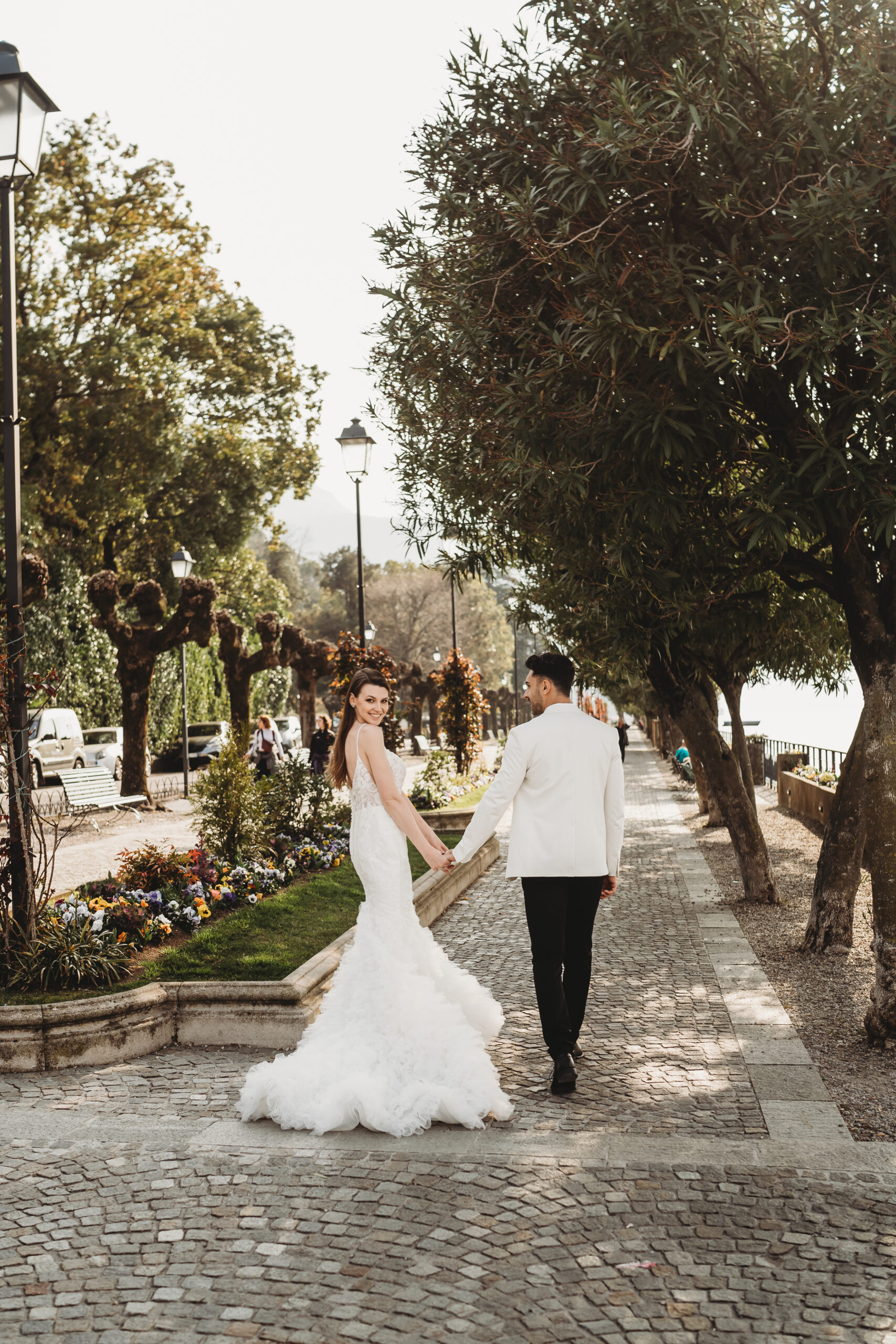 a bride and groom walking hand in hand down the promenade of lake como after their wedding