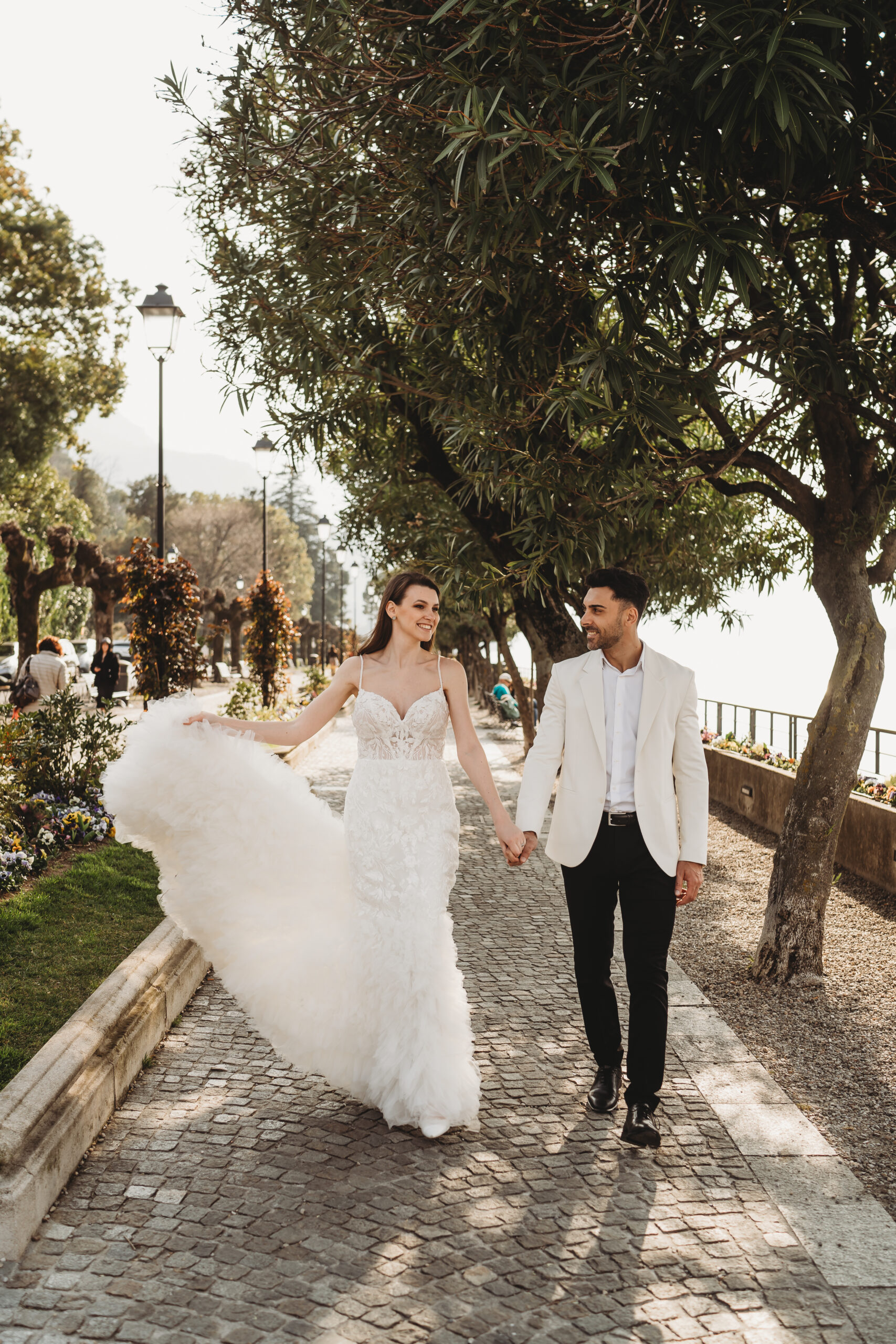 bride and groom walking holding hands as the bride plays with her dress