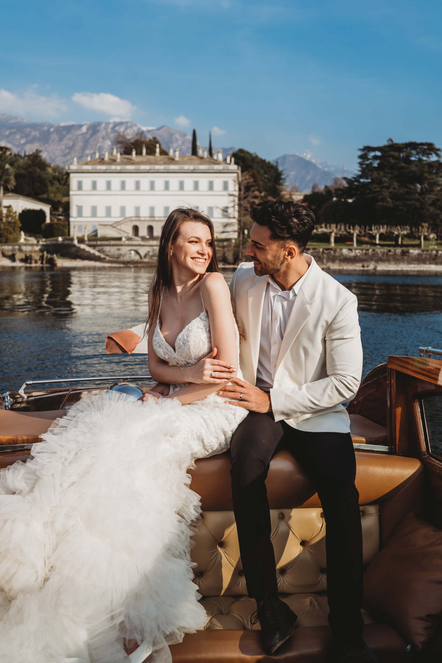 a newly wed couple laughing whilst on a boat across lake como