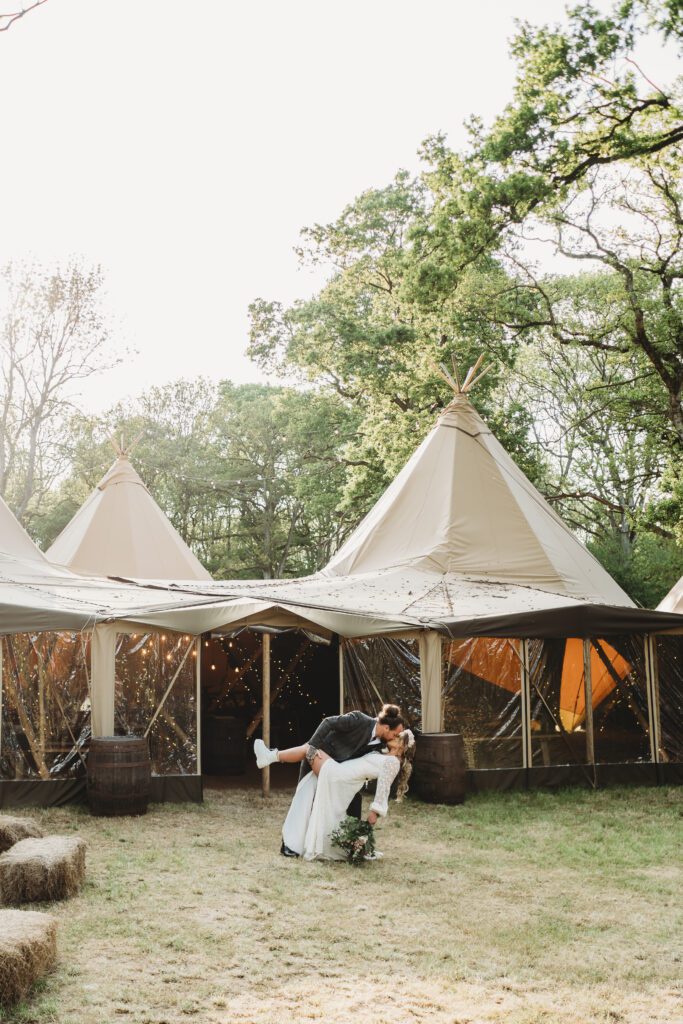 a bride and groom doing a drop kiss in front of Forest Edge's Tipis