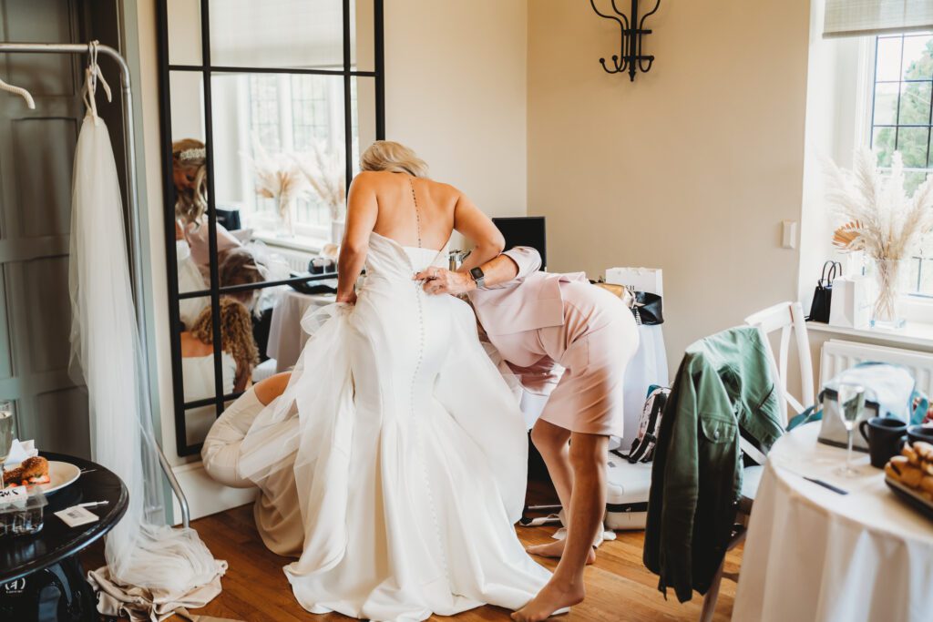 a bride getting into her dress before the wedding at the post barn berkshire 