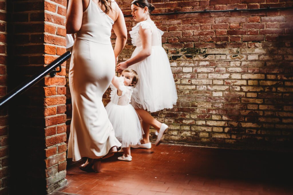 a flower girl looking back as shes lead away by 2 bridesmaids