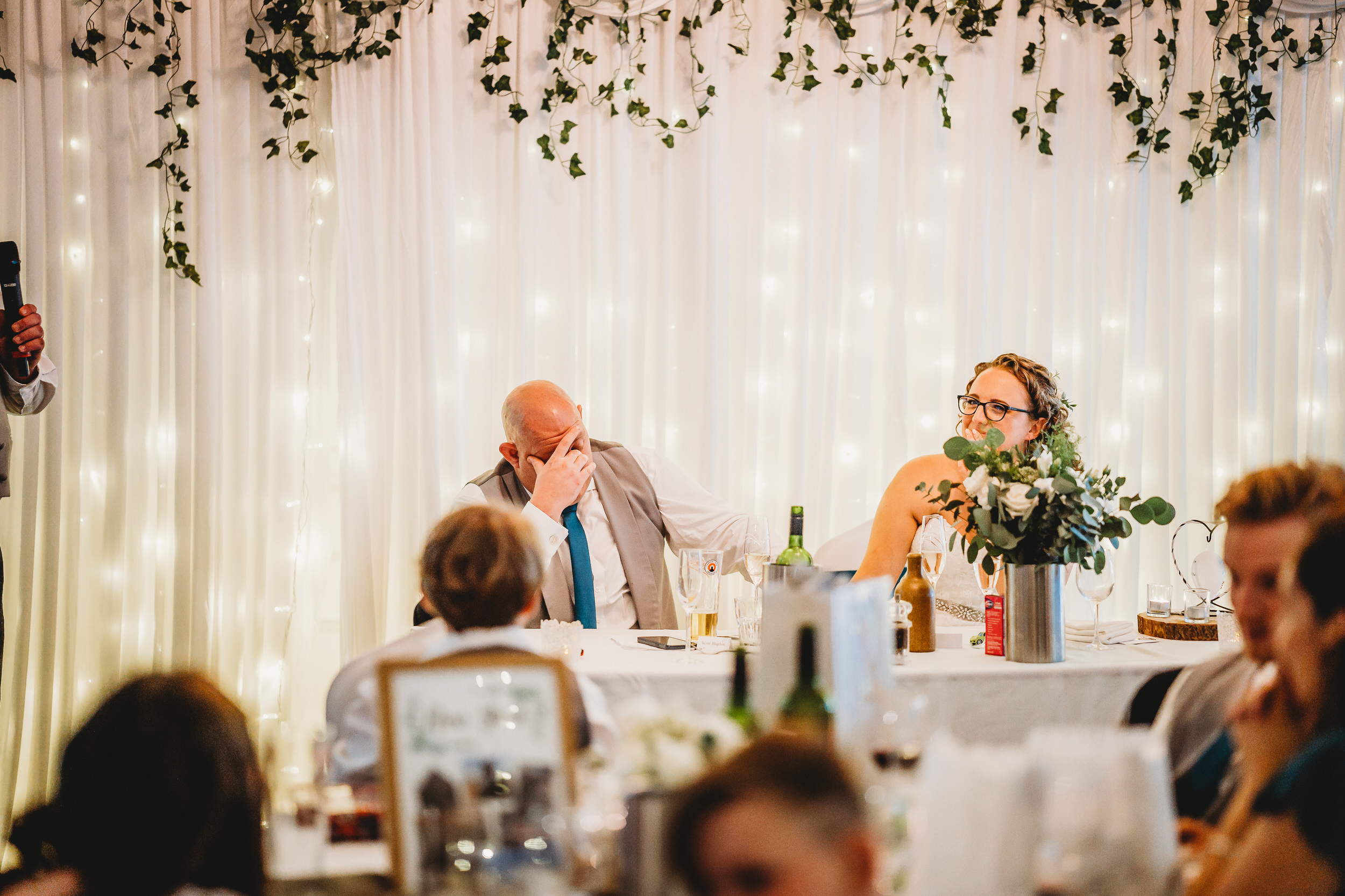 a groom holding his head in his hands during the best mans speech for a hampshire wedding photographer 