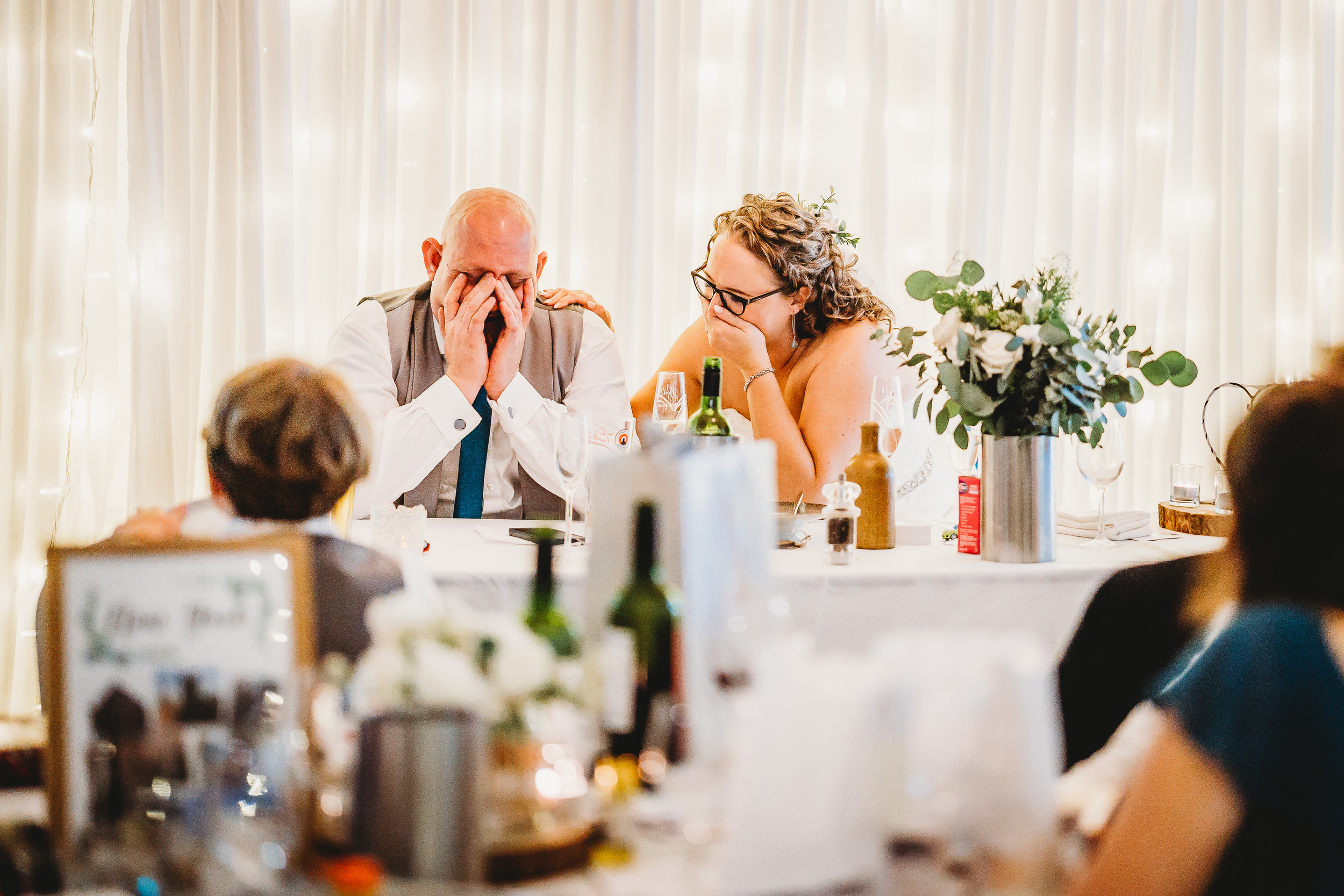 a bride and groom holding their heads in their hands during the best mans speech for a hampshire wedding photographer 