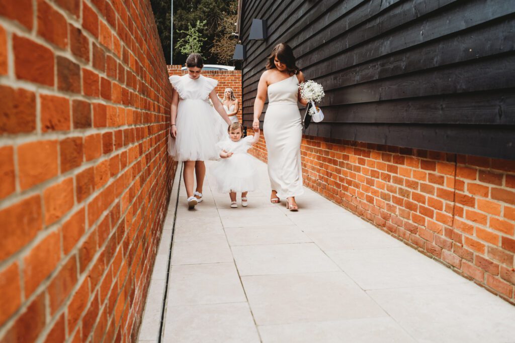 newbury wedding photography of a flower girl being led by 2 bridesmaids 