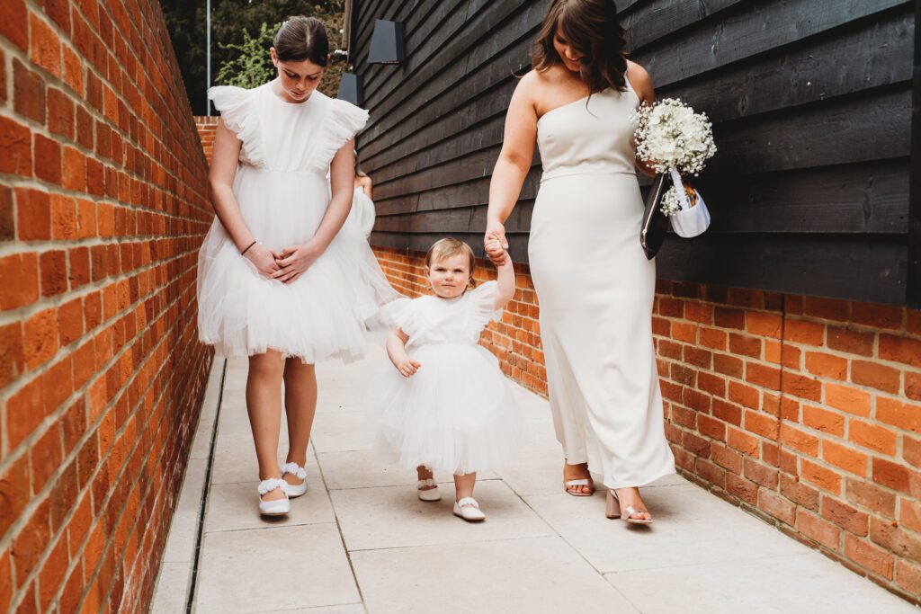 newbury wedding photography of a flower girl being led by 2 bridesmaids 