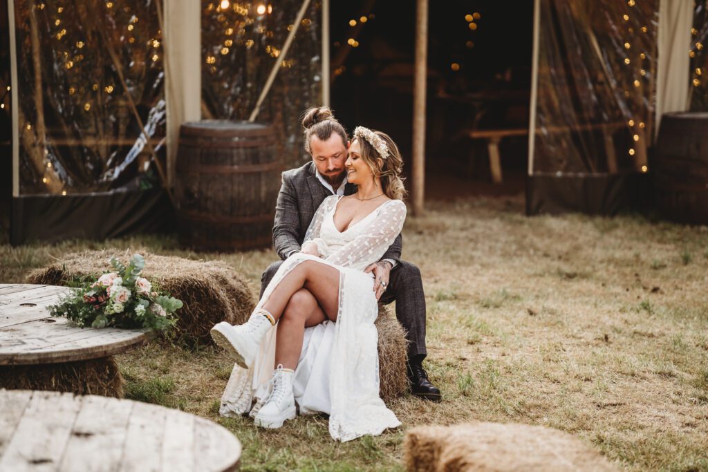 a bride and groom sat on hay bales after their festival themed wedding 