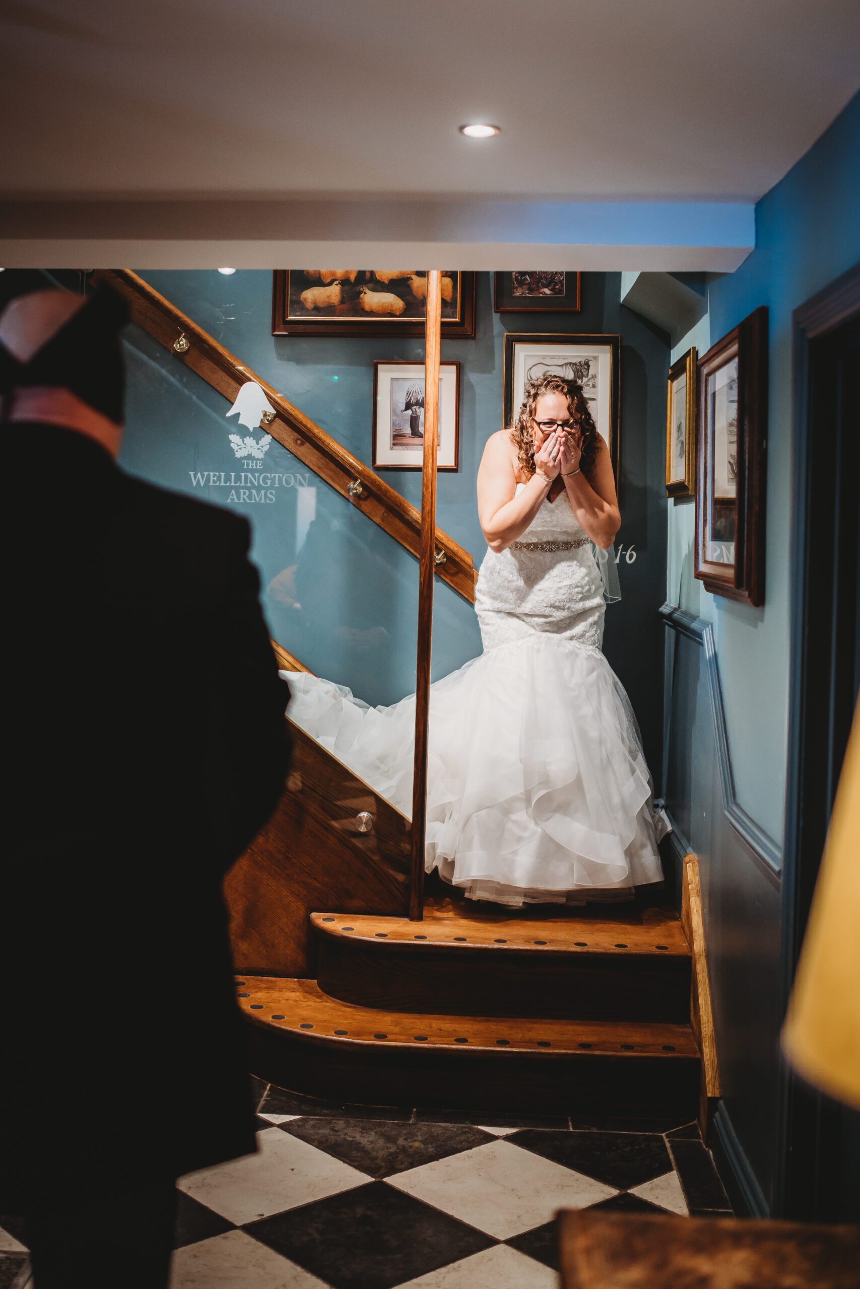 a bride clutching her face  in shock as she arrives at her blind look with her husband 