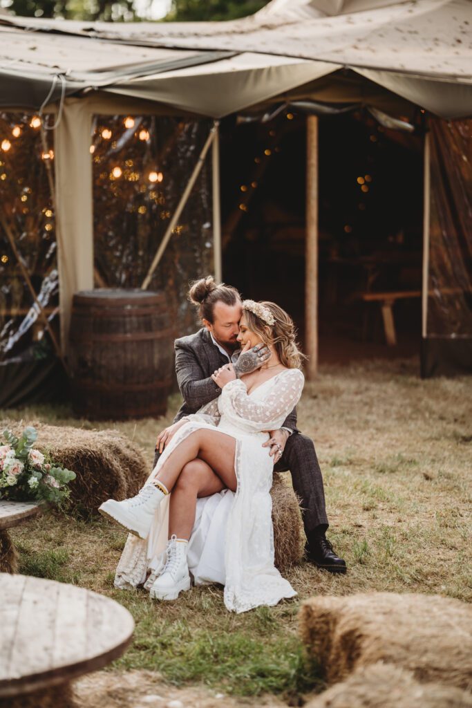 a bride and groom sat on hay bales after their festival themed wedding at a festival wedding venue 