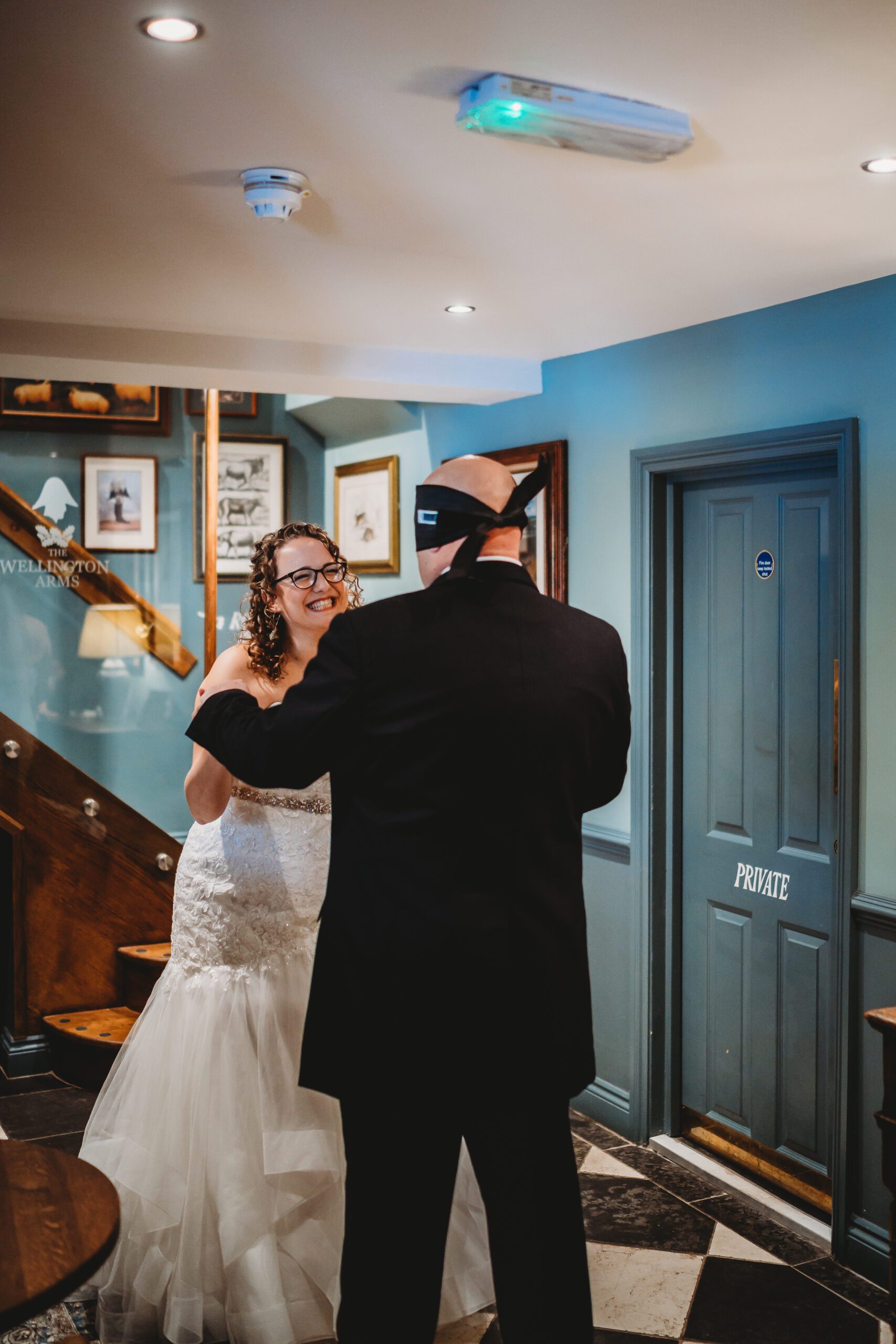 a bride smiling as she sees her husband for the first time whilst doing a  blind look