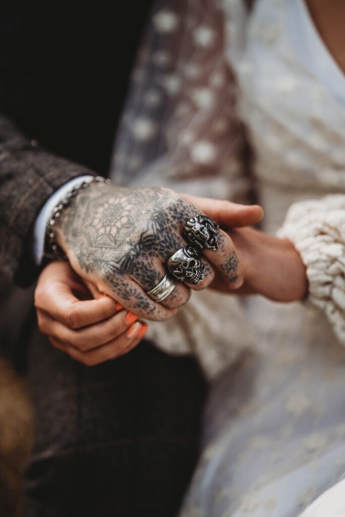 a tattooed grooms hand holding his new wifes hand