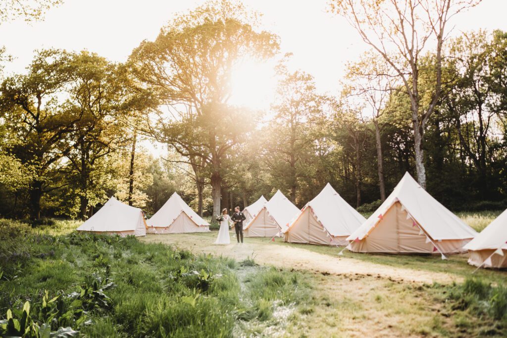 a bride and groom walking through bell tents at sunset following their festival wedding 