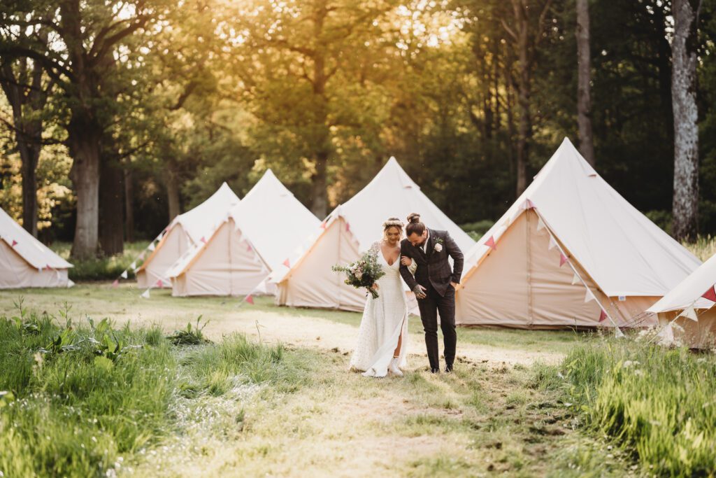 a bride and groom walking through bell tents at sunset for a festival themed wedding  