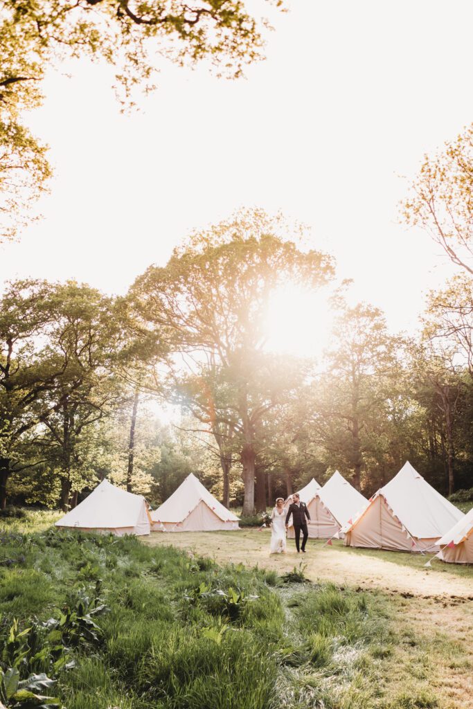 a bride and groom walking through bell tents at sunset following their festival wedding 