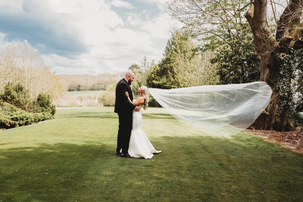 bride and groom cuddle as her veil gets taken by the wind