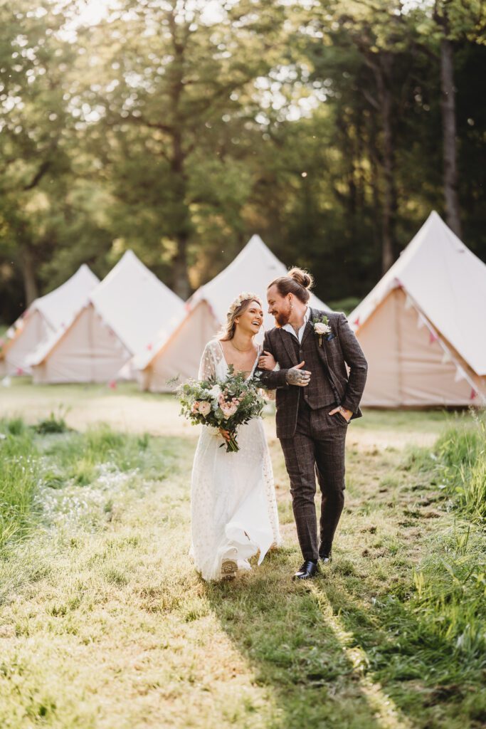 a bride and groom walking and chatting with the bell tents in the background at Woolley Park Estate