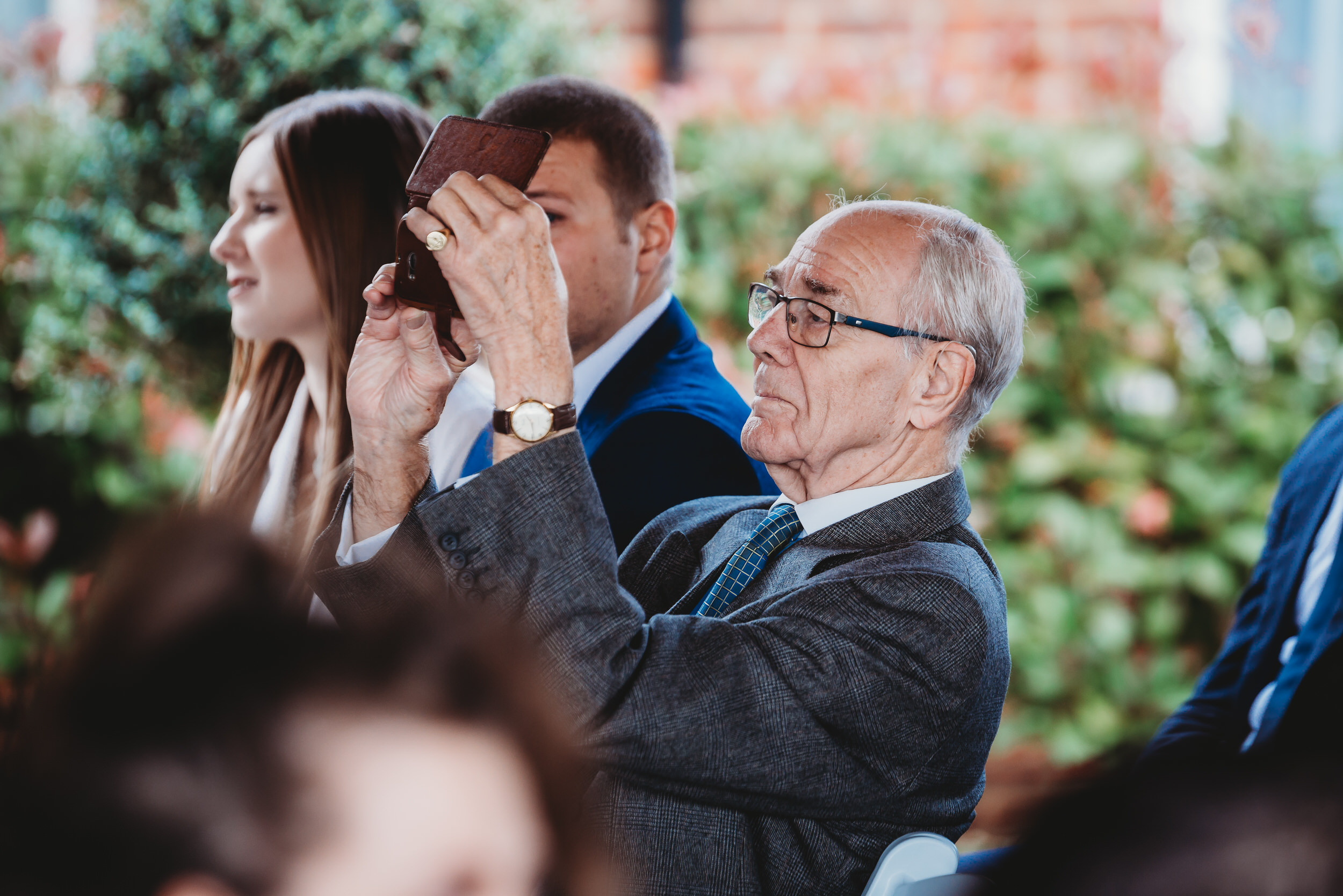 an elderly guest using his phone to take a picture during a wedding
