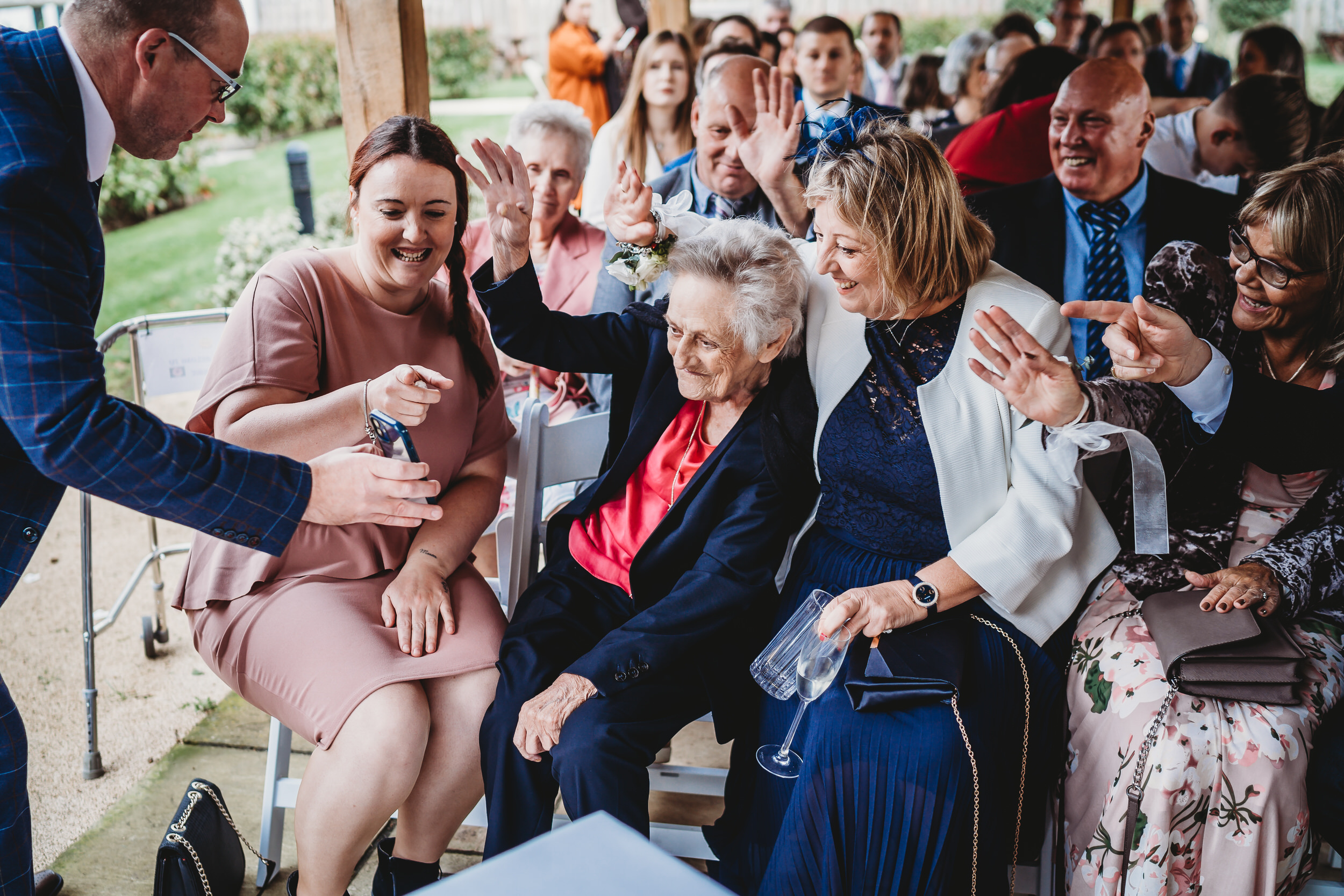 an elderly women waving to a person on face time during a wedding
