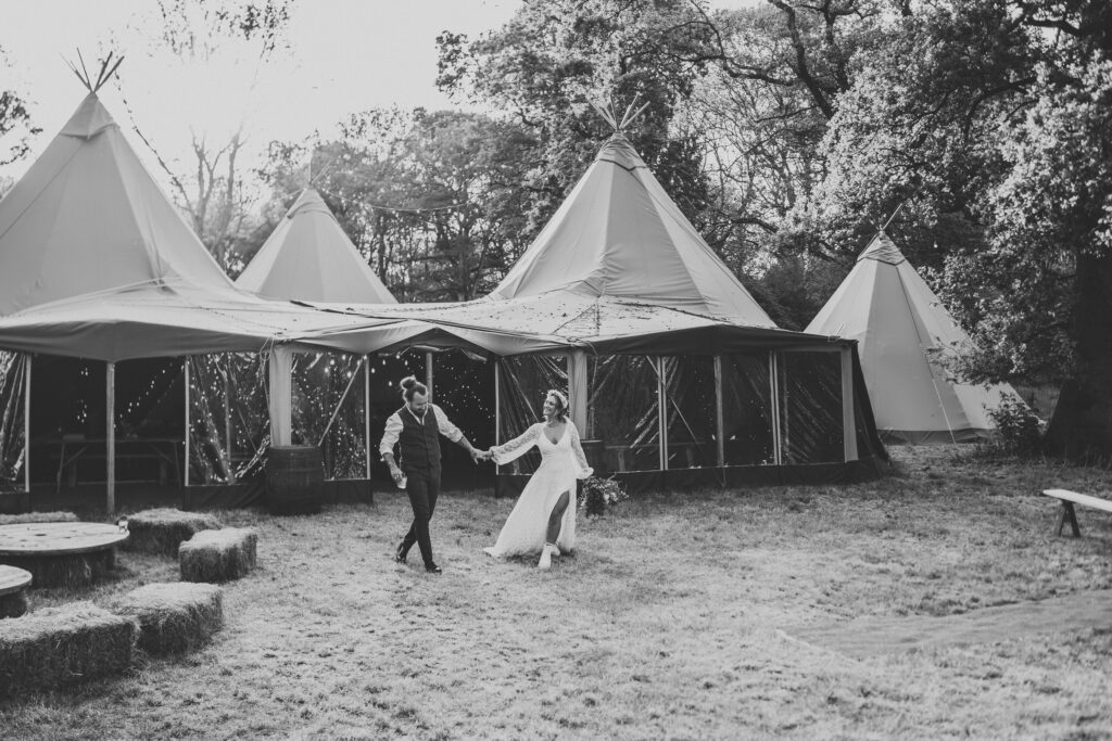 a black and white photo of a bride leading her new husband to the Forest Edge Tipis