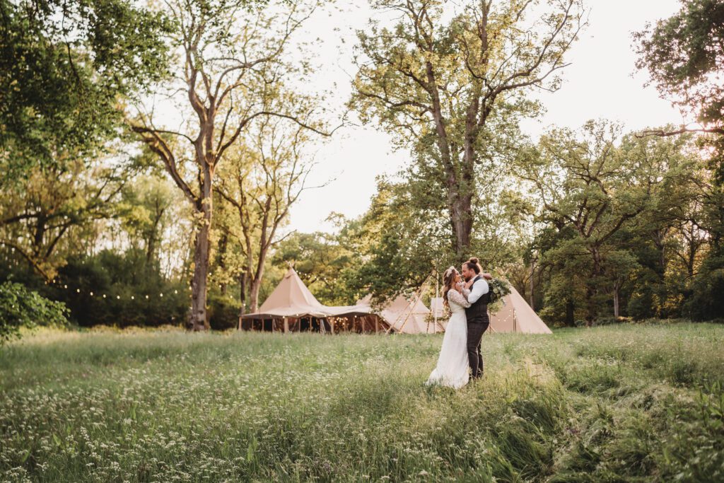 newly wed bride and groom cuddling with the tipis in the background for their festival wedding