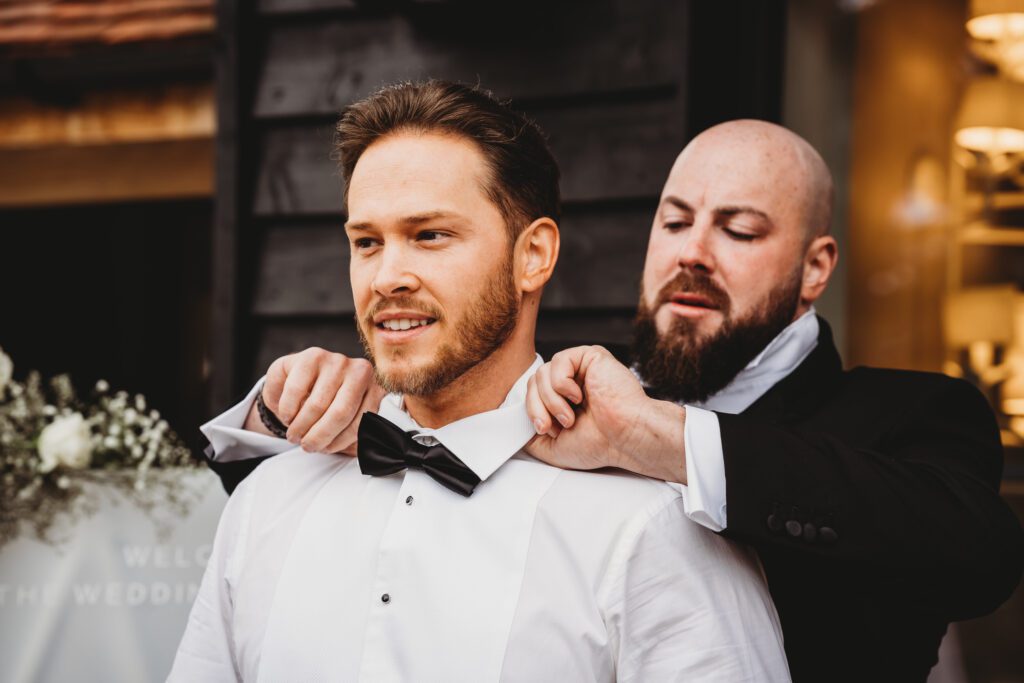 the groom helping his best man adjust his dickie bow tie as taken by a newbury wedding photographer 