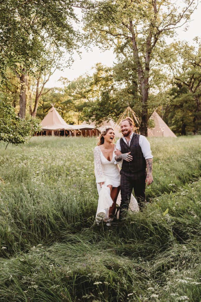 a bride and groom walking through long grasses and laughing for a festival wedding photographer